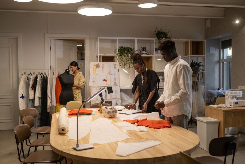 A small fashion design team laying out pattern pieces on a large table in a bright studio