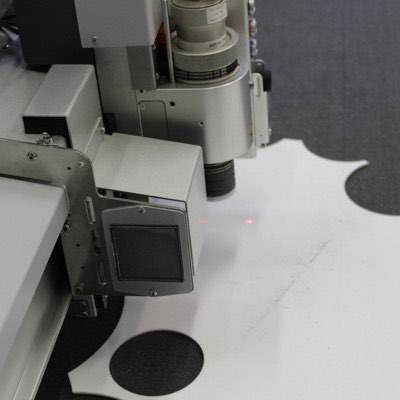 The head of a computerised cutting machine tracking across white fabric