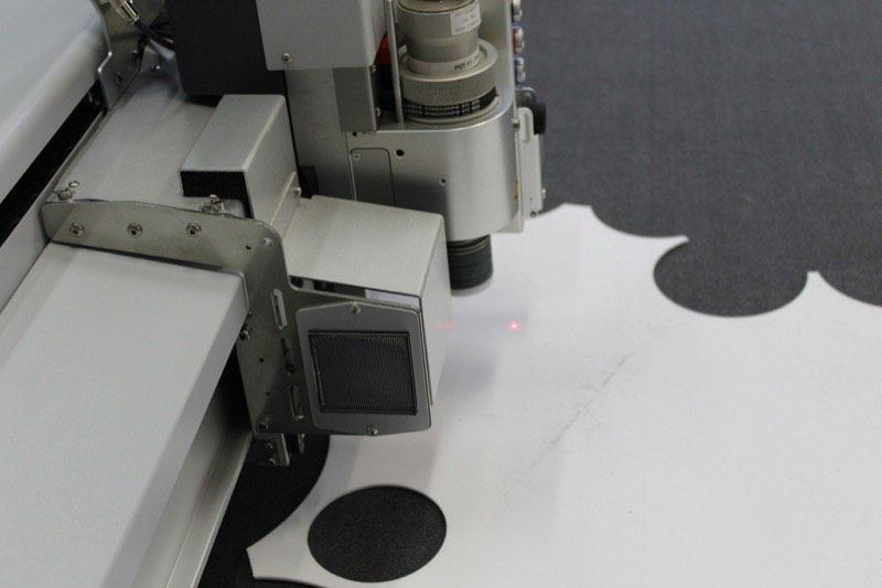The head of a computerised cutting machine tracking across white fabric