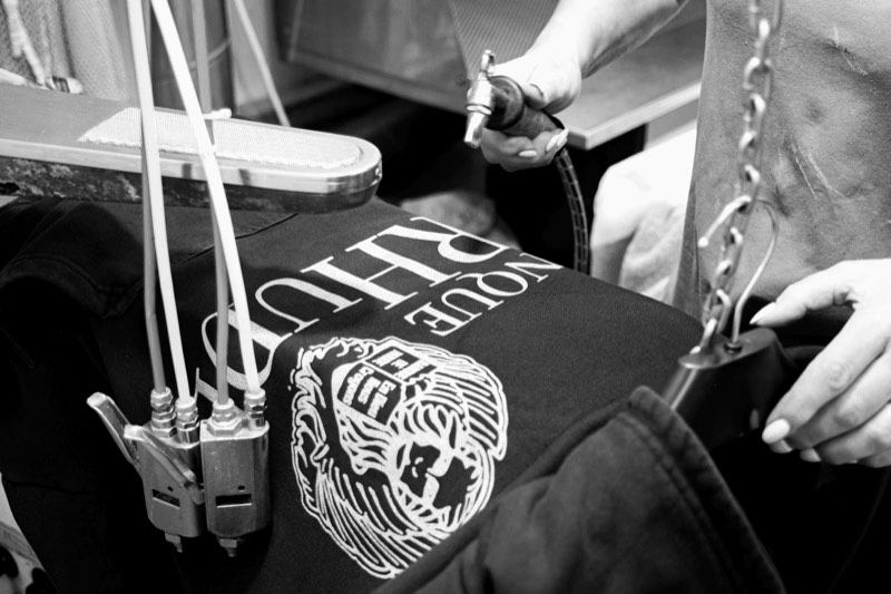 A heavyweight black t-shirt with a white screen print being inspected by hand