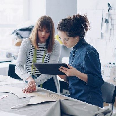 Two fashion designers reviewing a tablet over pattern pieces in a bright design studio