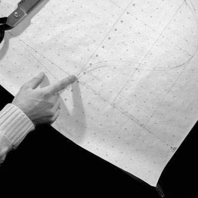 A hand pointing to drill marks on a laid-out pattern piece