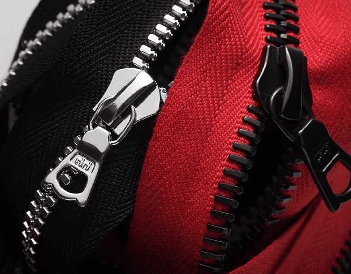 Two metal zippers side by side, one on black fabric and one on red