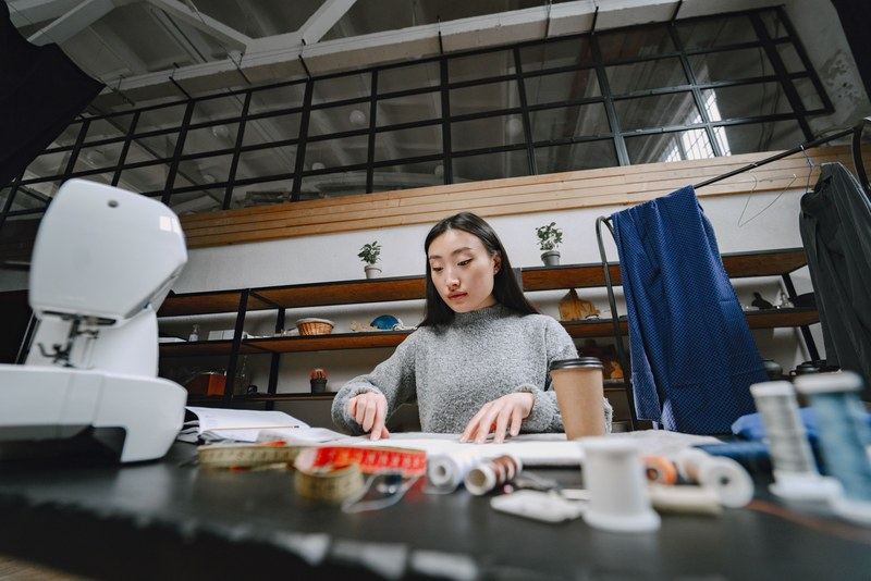 A fashion designer working at a studio desk surrounded by thread, tape measures and a sewing machine